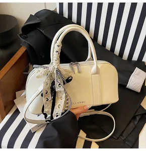 Detalle del bolso de charol blanco con logotipo y colgantes decorativos de encaje