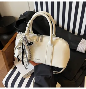 Detalle de bolso Boston blanco con lazo en el asa y letras de la marca Clear K