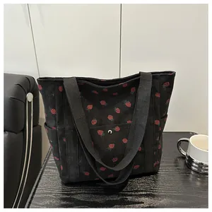 Close-up of strawberry print corduroy tote bag with front pocket and metal clasp detail