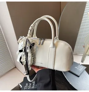 Detalle de bolso bowling de charol blanco crema con colgante de lazo de encaje y cremallera plata