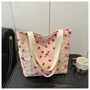 Detail of pink corduroy tote bag featuring red strawberry print and side pocket