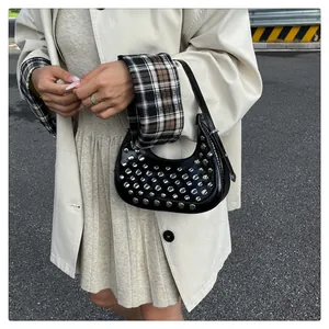 Detail of black crescent moon bag with silver rivets held by model in beige coat