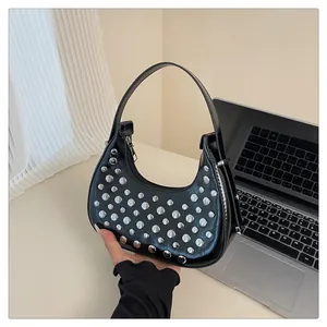 Close-up of black glossy leather crescent bag featuring silver punk stud decorations