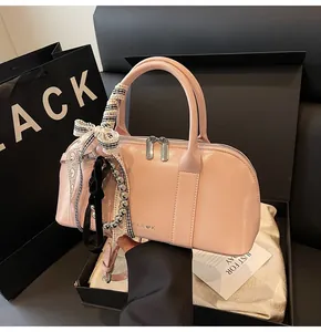 Vista de detalle del bolso cilíndrico rosa con lazos y colgantes en caja de regalo