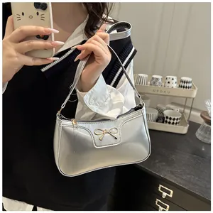 Silver mirror finish shoulder bag with golden bow accent shown in a mirror selfie