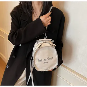 Detail eines perlmutt-silbernen Mini-Rucksacks mit Textdruck auf der Schulter