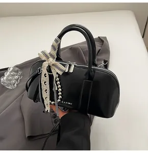 Detalle del bolso bowling negro con logo plateado, cadena de perlas y lazo de encaje