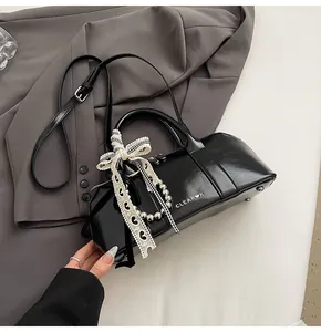 Detalle del bolso negro brillante con cadena de perlas y lazo de encaje fino