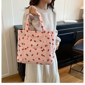 Detail of pink corduroy tote bag featuring red strawberry prints and front utility pocket