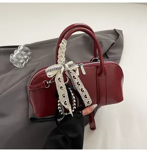Detalle de bolso burdeos con lazo de encaje blanco y doble cremallera metálica superior