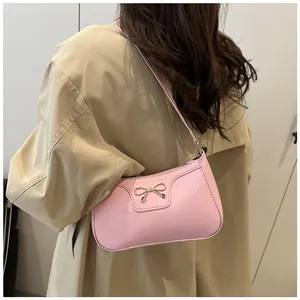 Pink patent leather underarm bag with a golden bow detail shown on shoulder