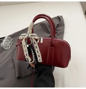Detalle de bolso en cuero charol burdeos con lazo de cinta y colgante de cuentas