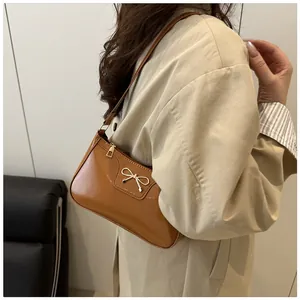 Detail view of a camel patent leather baguette bag with a gold metal bow on shoulder