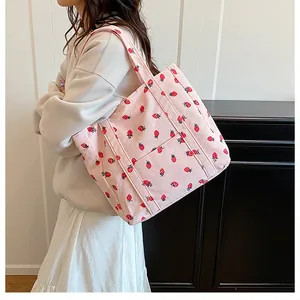 Detail of pink corduroy tote bag with red strawberry print and exterior pocket shown on model