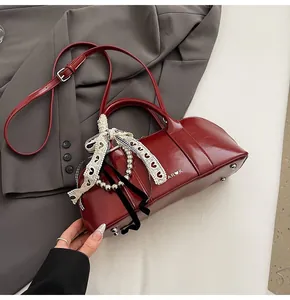 Detalle de bolso de cuero burdeos con lazo de encaje blanco y cadena de metal
