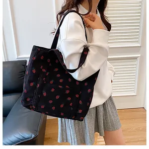 Detail of black corduroy tote bag with strawberry print worn by a model in interior