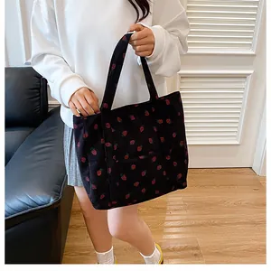 Close-up of corduroy tote bag featuring red strawberry patterns and front pocket