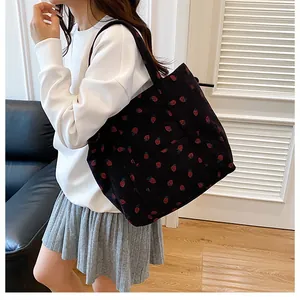 Detail of black corduroy tote bag featuring all-over red strawberry print patterns