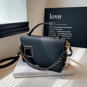 Bolso bandolera negro mate minimalista con cierre dorado sobre un libro de moda