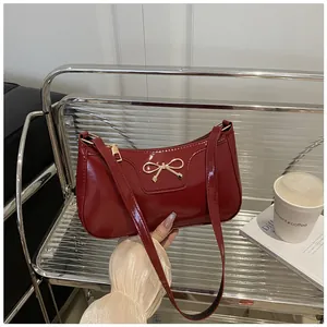Detailed view of red patent leather baguette bag with a gold bow buckle on metal grid