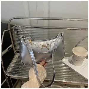 Macro detail of silver metallic underarm bag with decorative golden metal bow knot