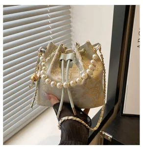 Detail of blue and gold jacquard bucket bag featuring elegant large pearl handle and metal chain