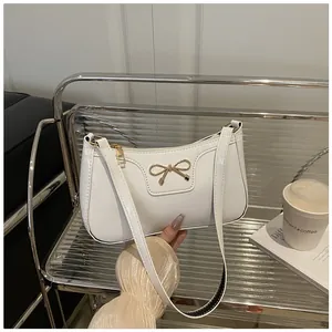 Detail of white patent leather shoulder bag with a gold metal bow on a moon crescent shape
