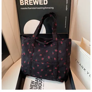 Close-up of black corduroy tote bag with strawberry patterns and a front pocket