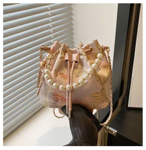 Detail of pink satin bucket bag with floral embroidery and pearl handle accent