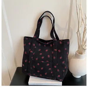 Close-up of black corduroy tote bag with red strawberry embroidery on a book