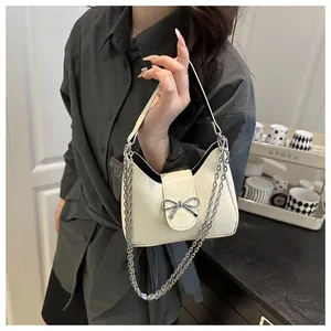 Détail d'un sac sous le bras blanc crème avec un nœud en métal argenté et une chaîne