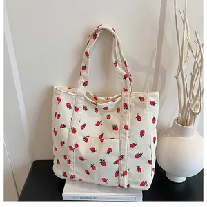 Detail of strawberry print corduroy tote bag with front pocket on a book setup