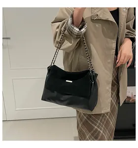 Detail of black leather chain shoulder bag shown on model with chic beige trench coat