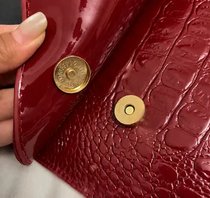Detail of red crocodile textured patent leather bag featuring a secure magnetic clasp closure