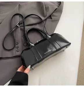 Detalle del bolso cilíndrico negro brillante con herrajes plateados y logo blanco impreso