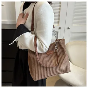 Detail of corduroy tote bag with brown leather chain strap on model's shoulder
