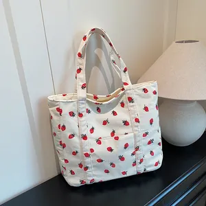 Corduroy tote bag with strawberry prints and a front pocket on a minimal desk
