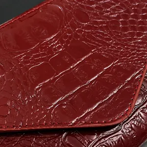 Macro shot of dark red crocodile embossed leather with glossy finish and fine stitching