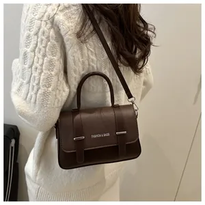 Détail d'un sac boîte en cuir marron foncé avec texture grainée et boucles argentées