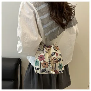 Detail of floral embroidery linen bucket bag with pearl drawstring and golden chain strap