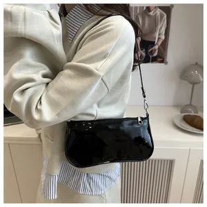 Close-up of a glossy black patent leather baguette shoulder bag worn by a model