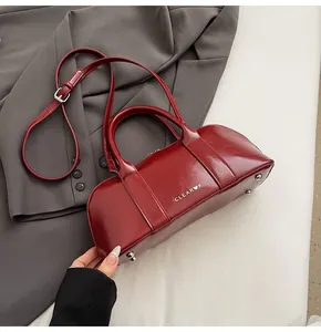 Detalle de bolso de cuero brillante burdeos con logotipo plateado sobre blazer gris