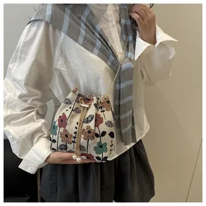 Detail of floral embroidery on linen bucket bag with elegant pearl drawstring and gold chain