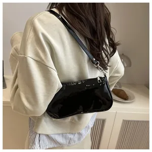 Close-up of black glossy patent leather baguette bag with silver zipper on model