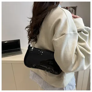 Detail of a black patent leather baguette bag with silver zipper on a white cabinet