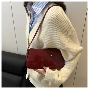 Close-up of a burgundy patent leather underarm bag with glossy finish on a model