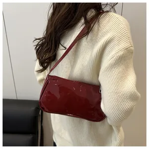 Detail of glossy burgundy baguette shoulder bag worn over a cream knitted sweater