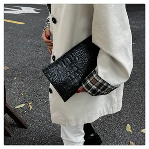 Detailed close-up of a black crocodile-embossed leather envelope bag held by a model