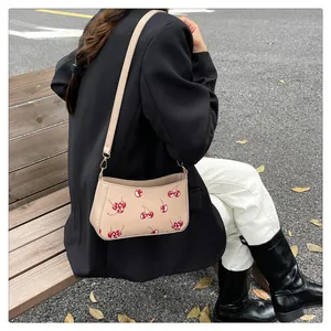 Beigefarbene Schultertasche mit Kirschmuster getragen von Model in einer Parkanlage
