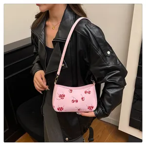Nahaufnahme einer rosa Umhängetasche mit Kirschdruck, getragen von einem Modell in Lederjacke